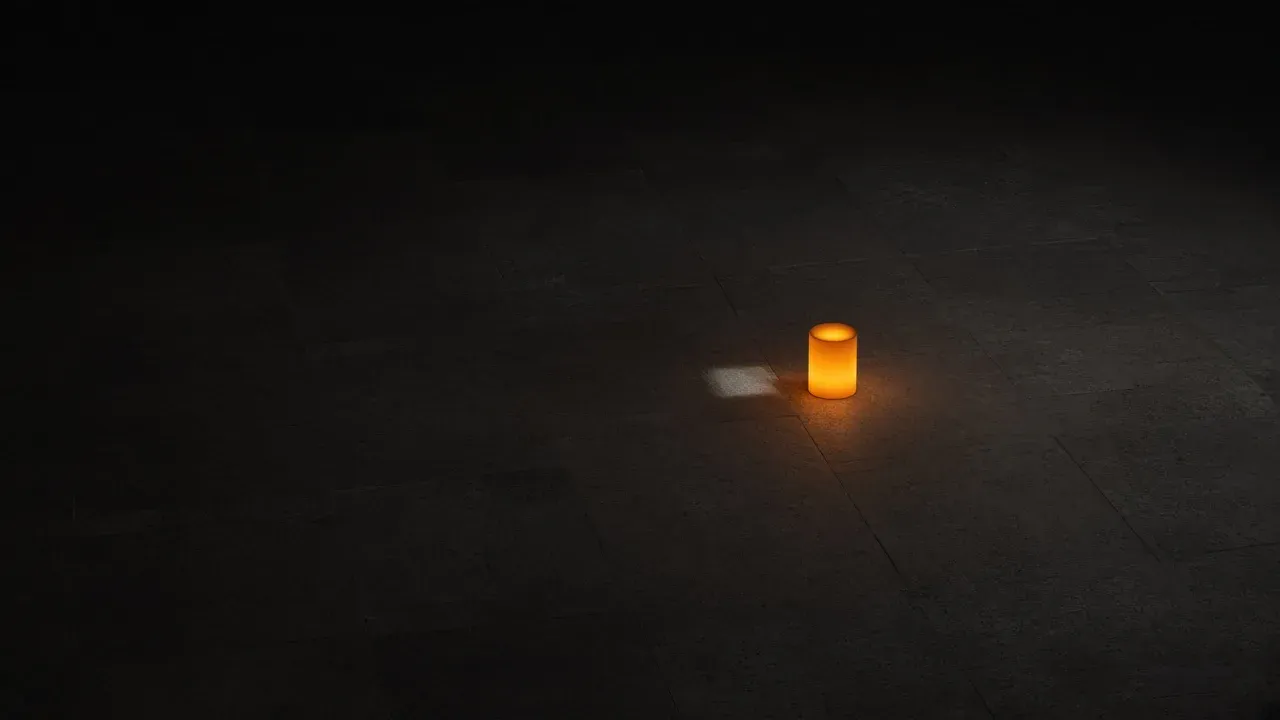 A small glowing amber cylinder on a dark tiled floor, with a short patch of light beside it and empty darkness around it