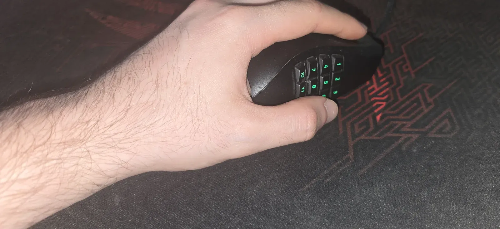 Side view of a left hand holding the Razer Naga Left-Handed, thumb over the 12-button grid and ring and pinky fingers resting on the side support