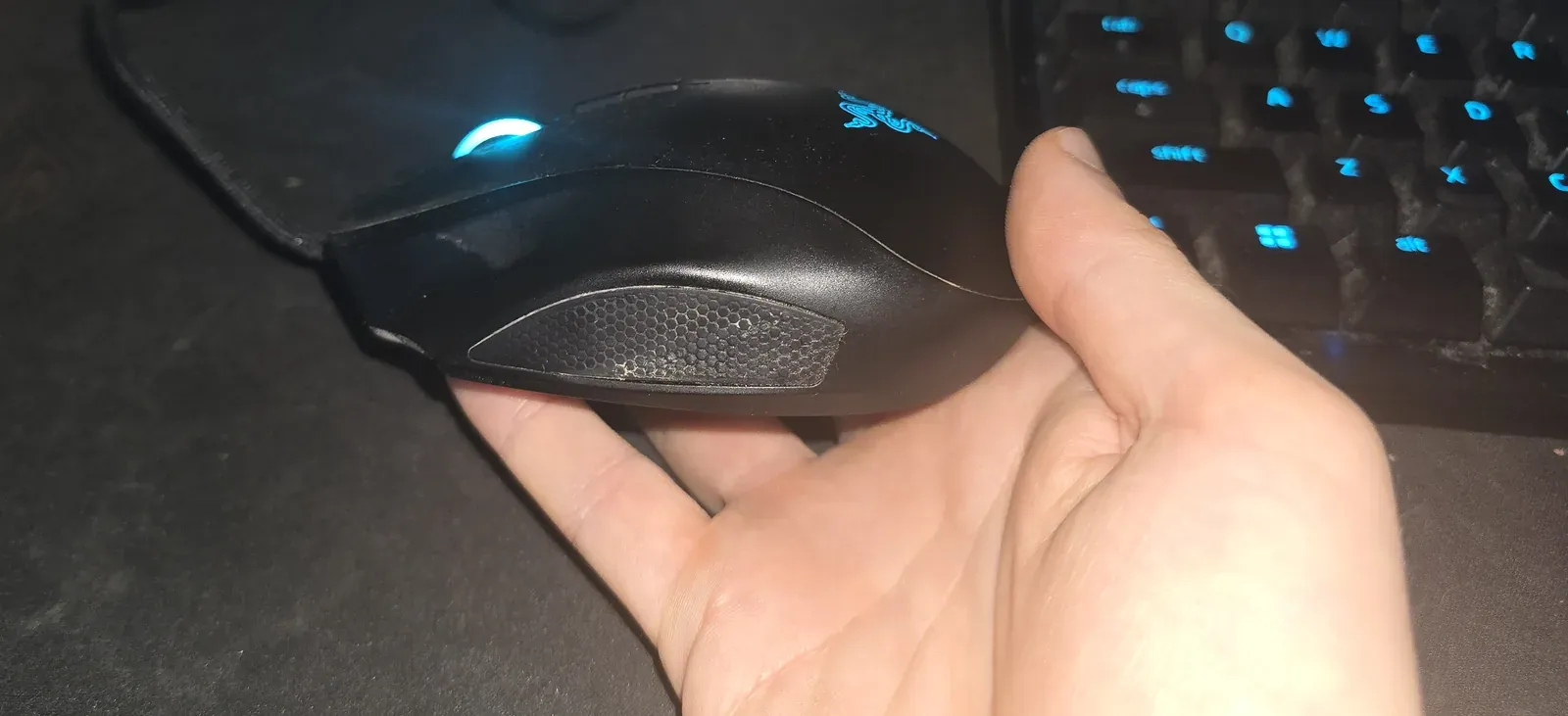 Left hand holding the Razer Naga Left-Handed, showing the honeycomb-textured grip patch on the left side where the ring finger and pinky rest