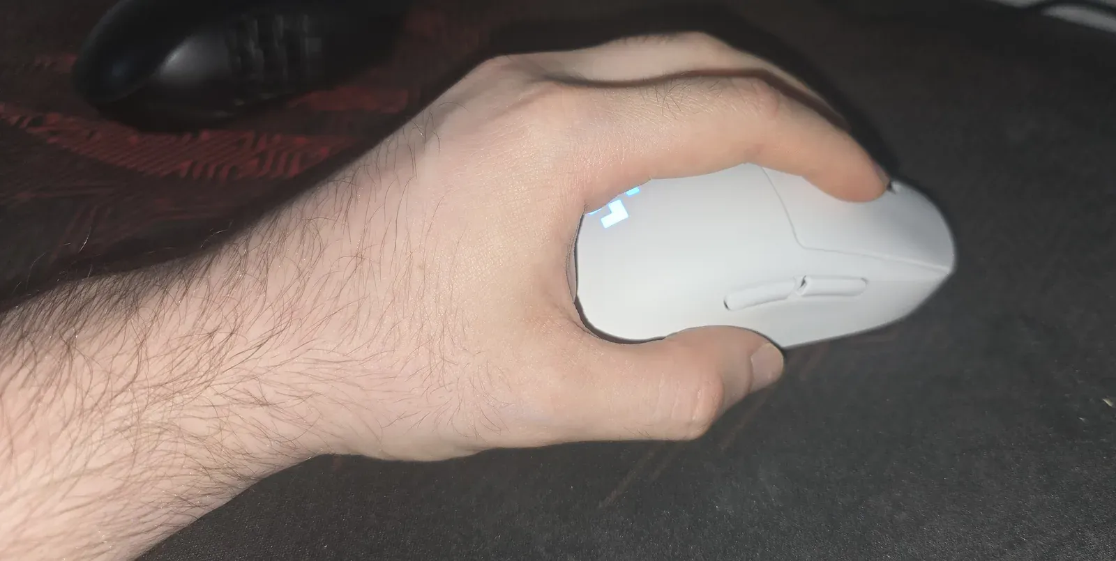 Side view of a left hand holding the white Logitech PRO 2 LIGHTSPEED, thumb resting on the right-side buttons