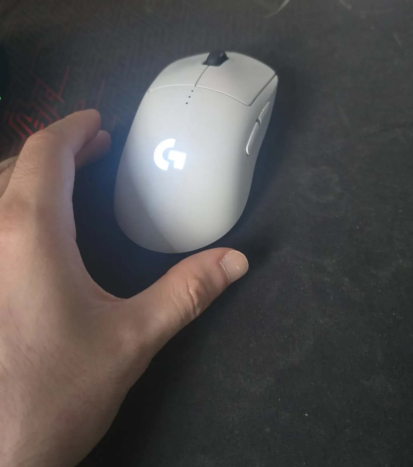 Top view of the white Logitech PRO 2 LIGHTSPEED with its G logo lit, a left thumb on the right side