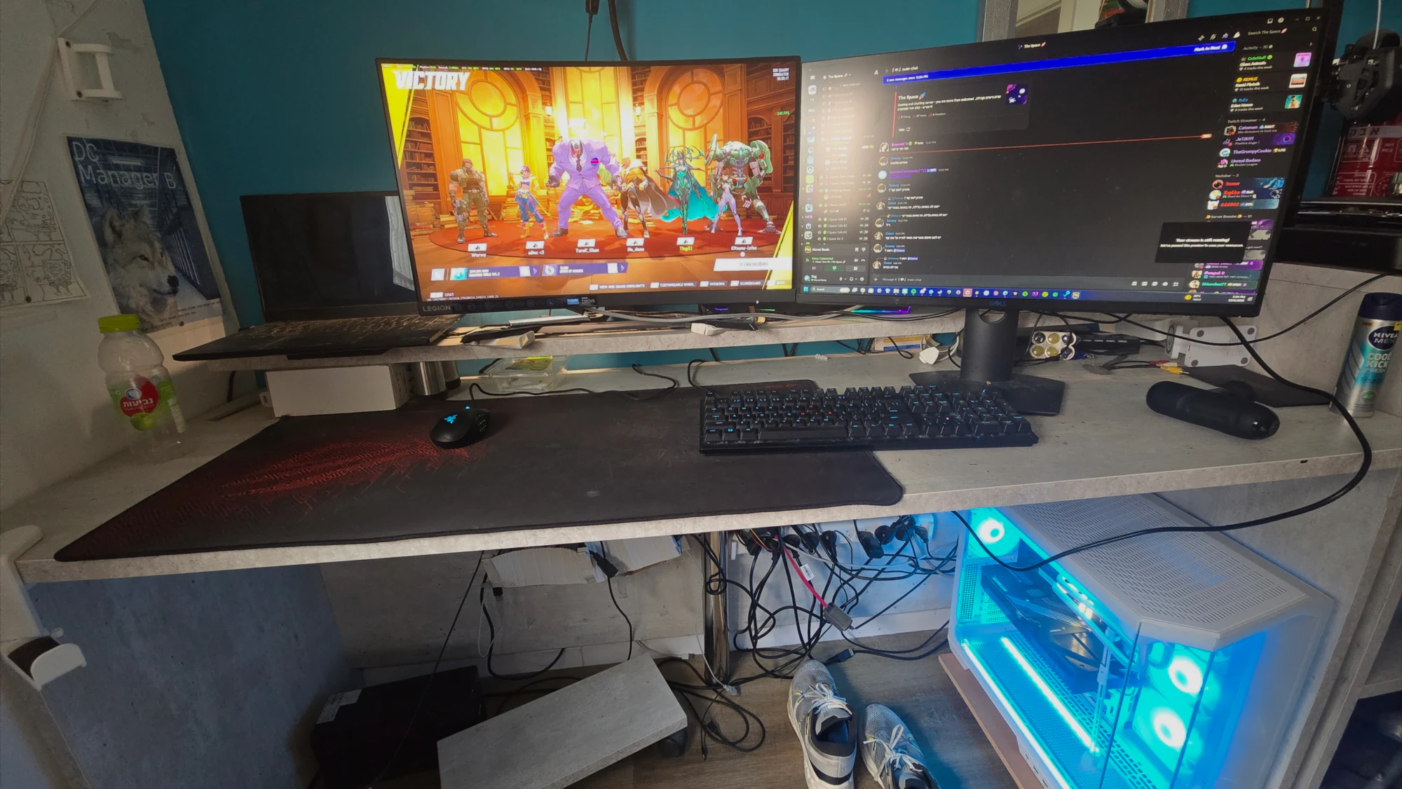 Yuval's dual-monitor desk: an Overwatch victory screen on the left display, a desktop on the right, keyboard and mouse on a large pad, and a white PC glowing under the desk